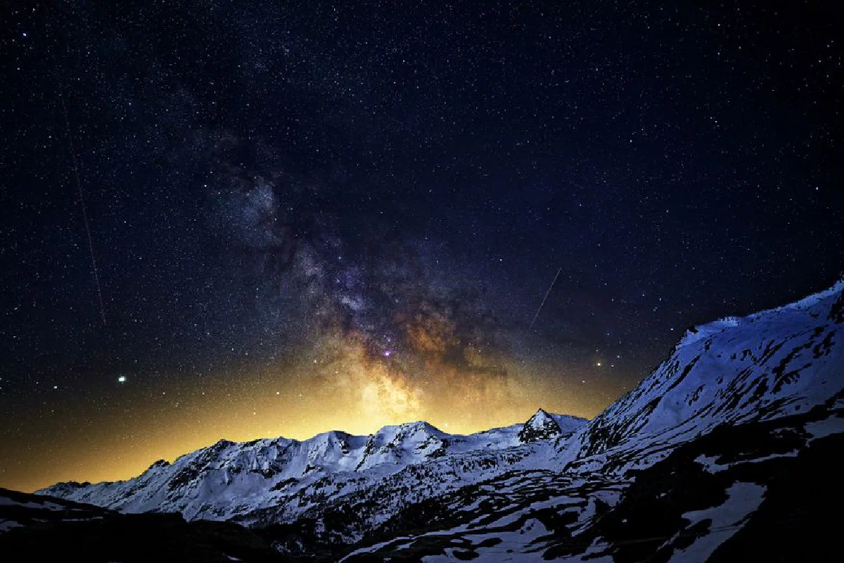 The Milky Way illuminates a snowy mountain landscape under a star-filled night sky.