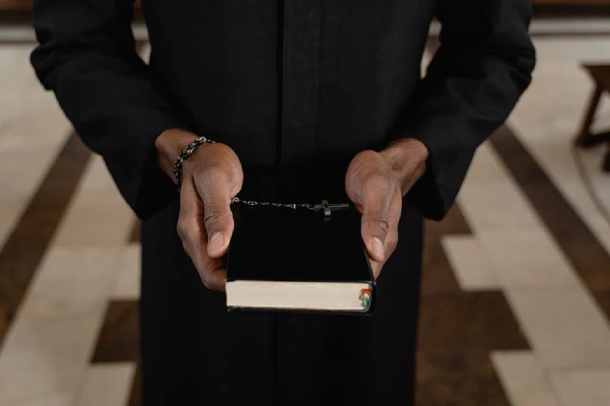 A priest's hands holding a Bible and rosary beads, symbolizing faith.