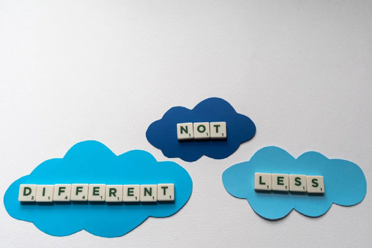 Inspiring autism awareness message using Scrabble tiles on blue paper clouds.