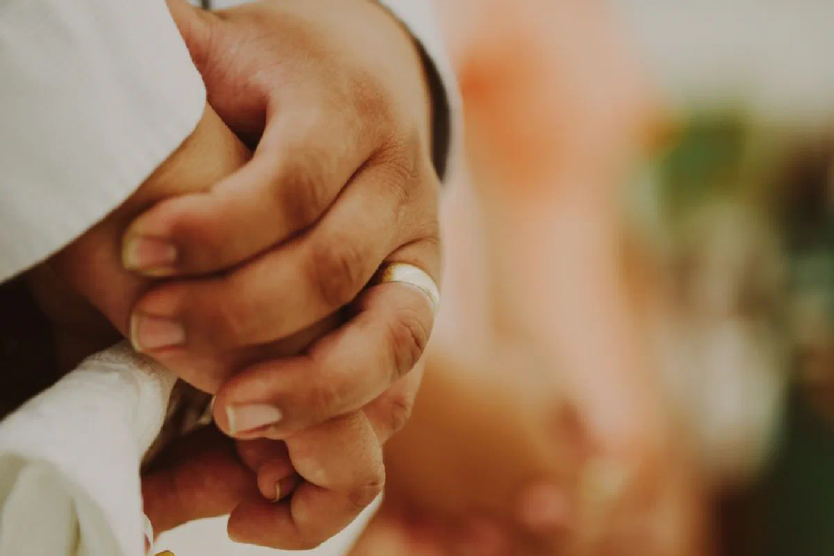 Warm close-up image of hands in loving embrace, showcasing a wedding ring.