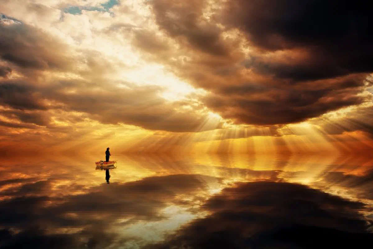 A lone boat floats on calm waters under a dramatic and vibrant sunset sky, casting reflections.
