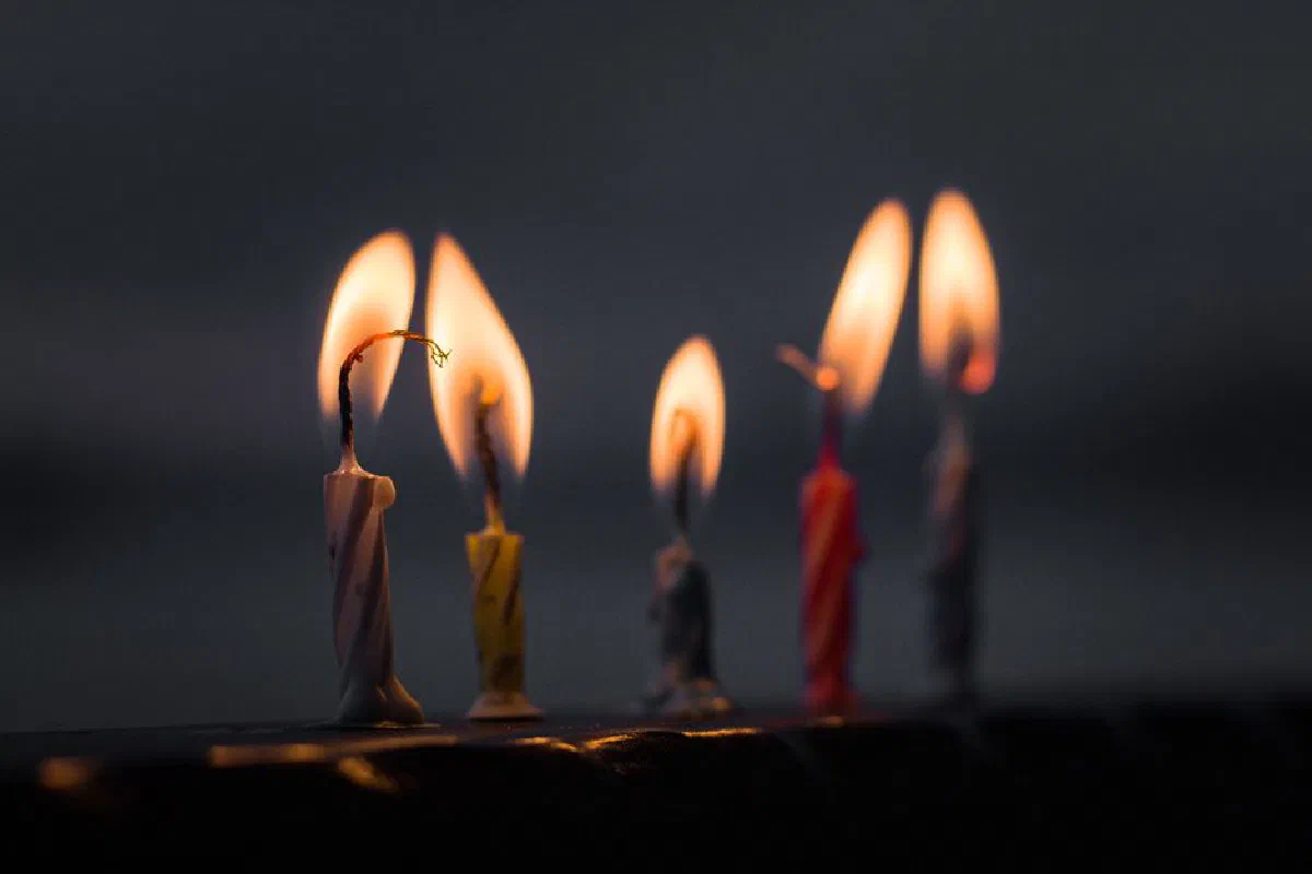 Close view of five burning birthday candles in the dark with colorful wax.