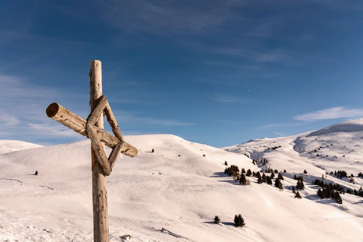 Scenic snowy mountains under clear blue sky with wooden cross.