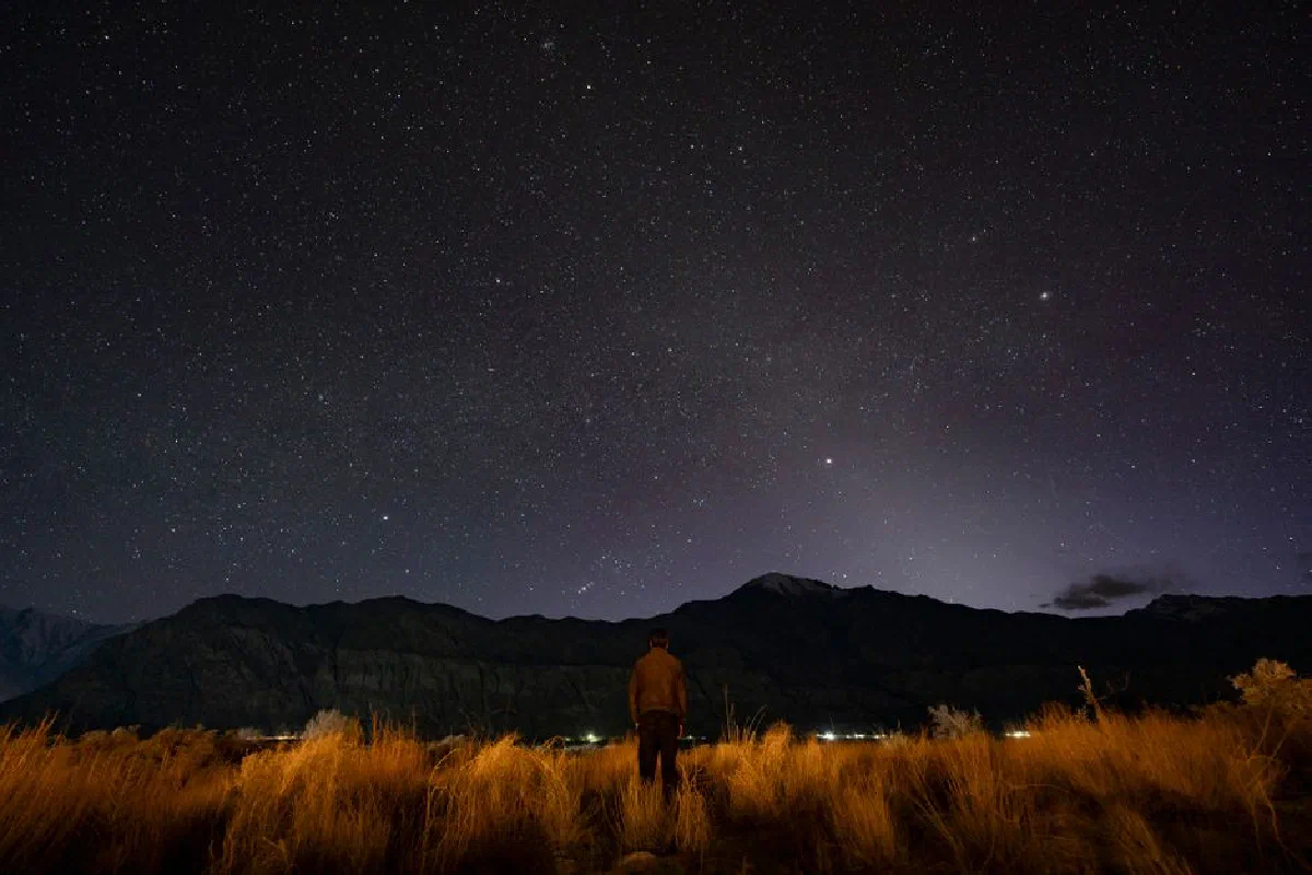 A person gazing at a star-filled night sky with mountainous silhouettes. Perfect for nature and astronomy themes.