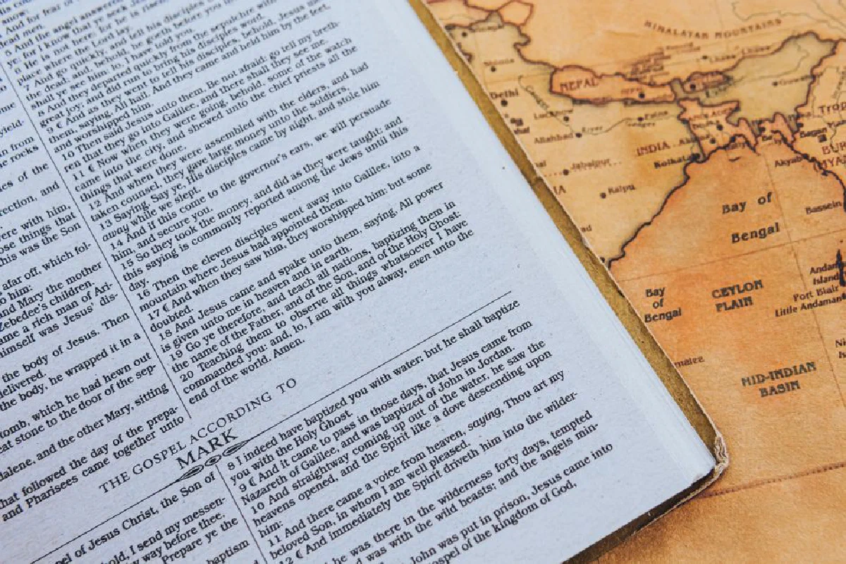 Photo of an open Bible page next to a vintage map. Historical and religious themes.
