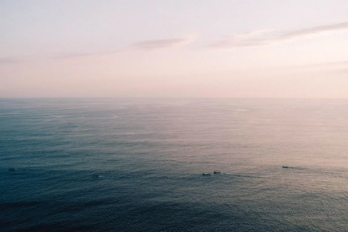 Tranquil seascape with distant boats on the horizon at dawn, featuring calm waves and soft morning light.