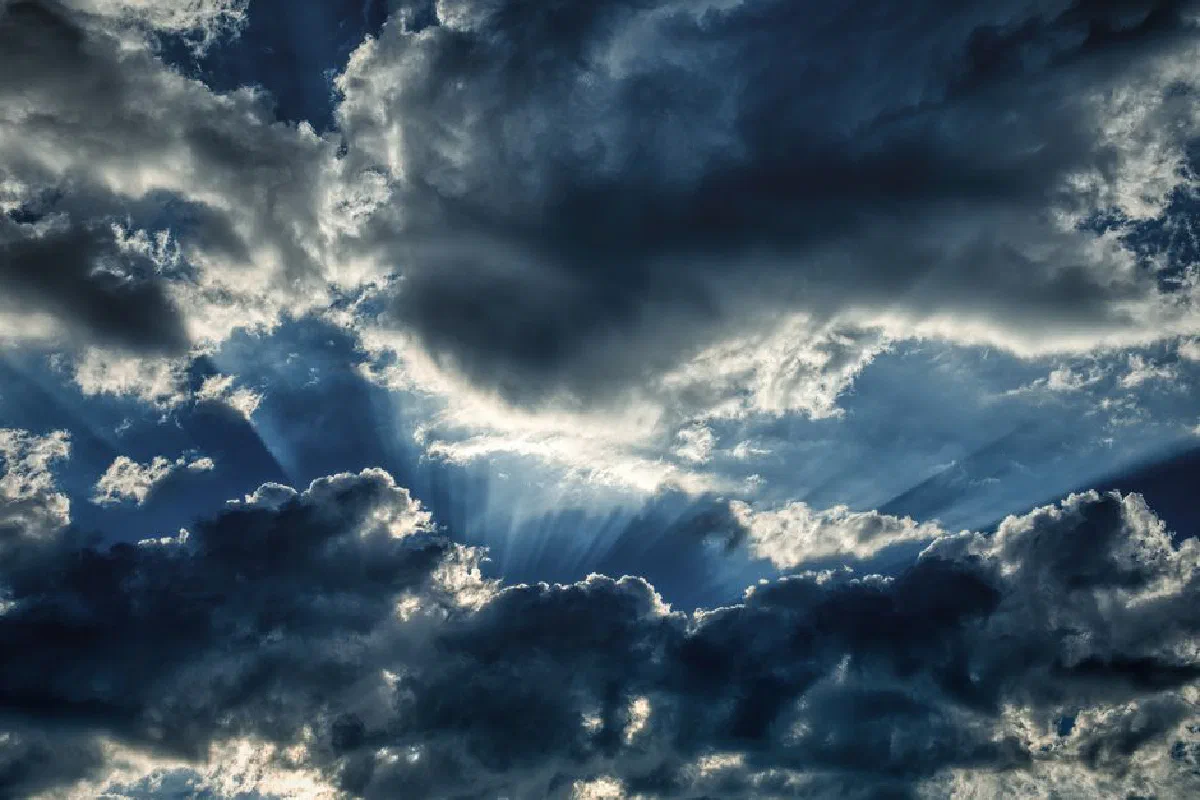 Dramatic sky with sun rays piercing through dark storm clouds, creating a cloudscape.
