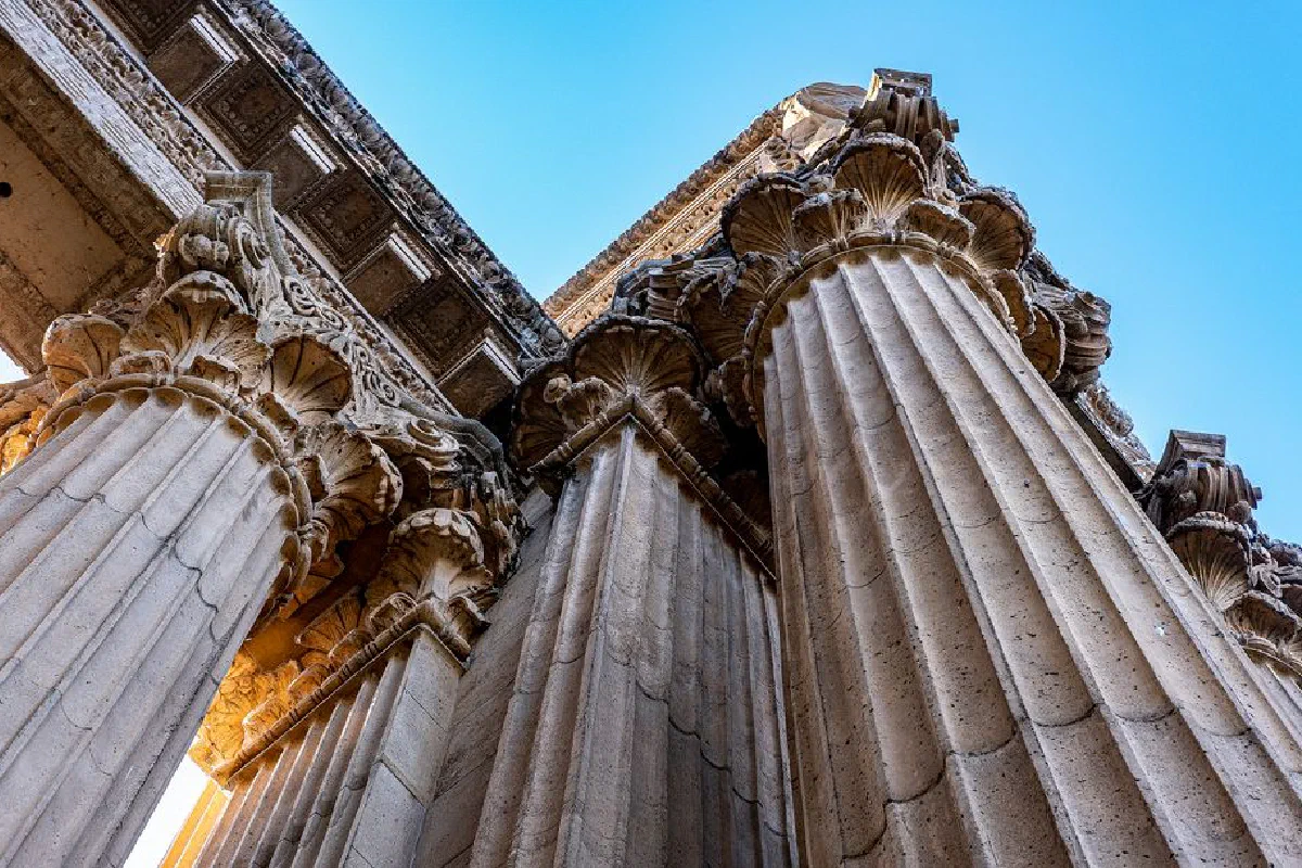 Upward view of intricate classical columns under a clear blue sky.
