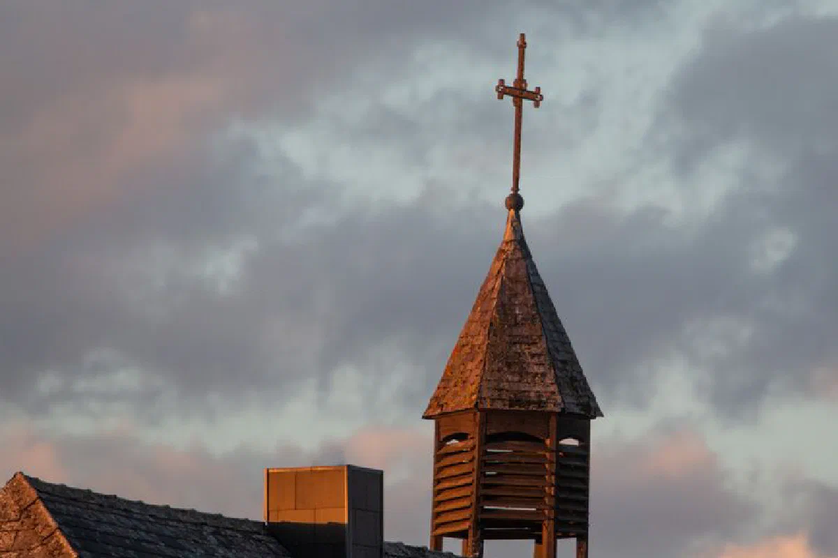 Wooden bell tower with cross silhouetted against a colorful dawn sky. Peaceful and serene.