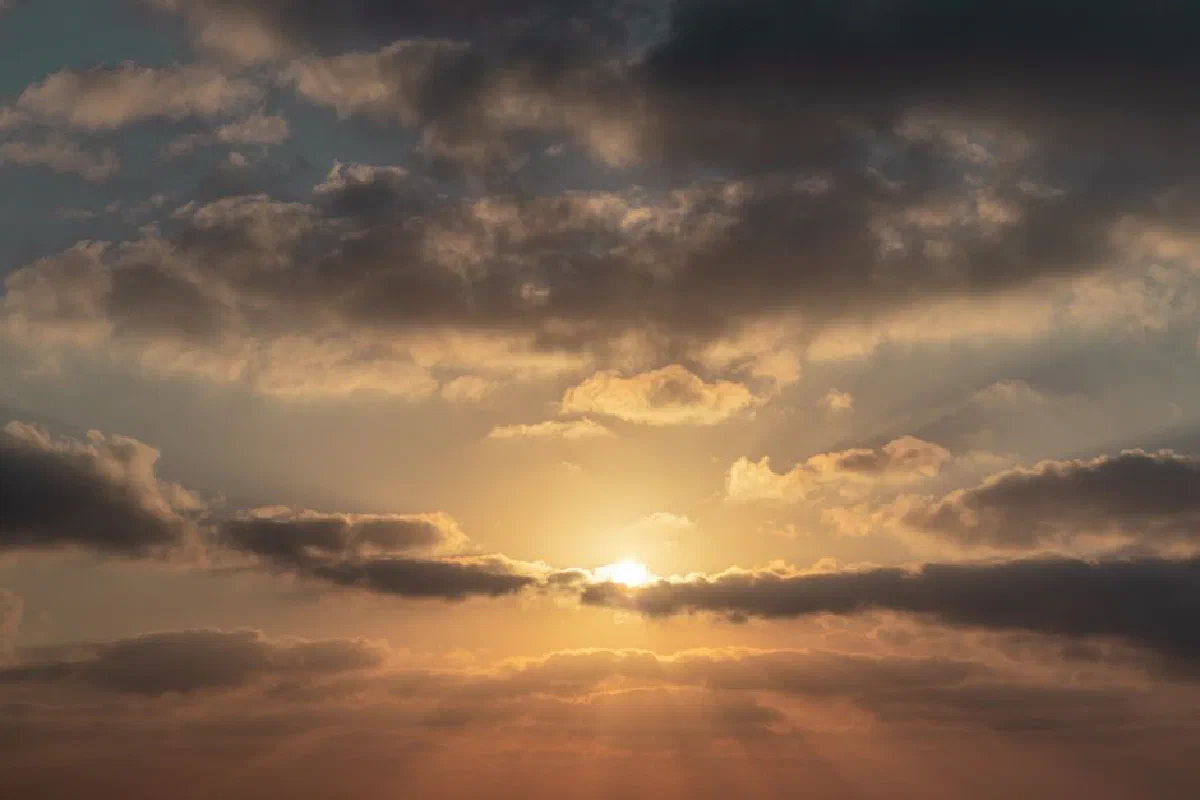 Picturesque view of fluffy clouds floating over calm blue sky with sun shining at sunrise