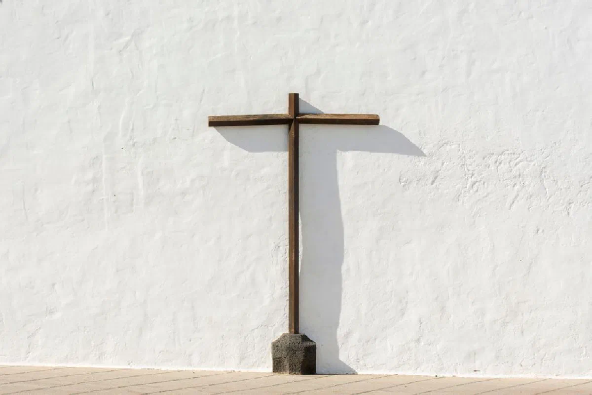 A simple wooden cross standing against a stark white wall, symbolizing faith and tranquility.
