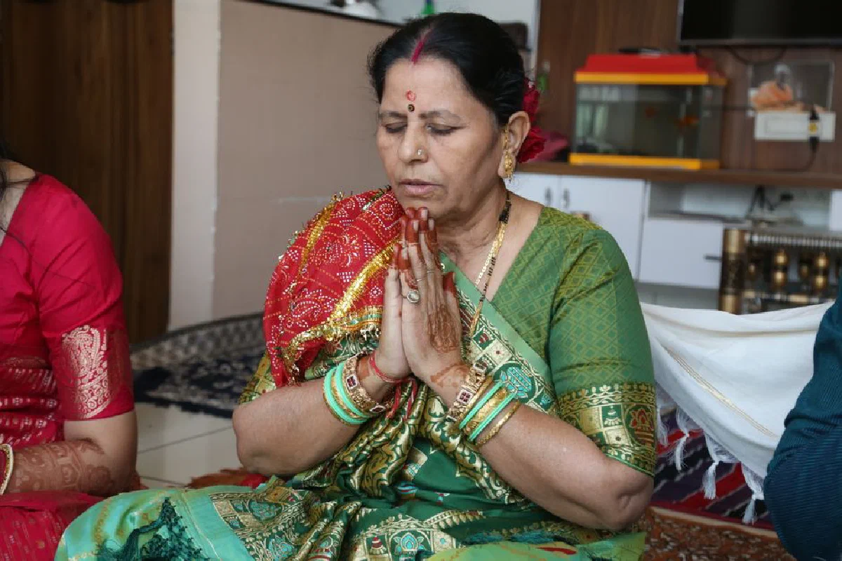 Indian woman in traditional attire praying during a pooja ceremony indoors.