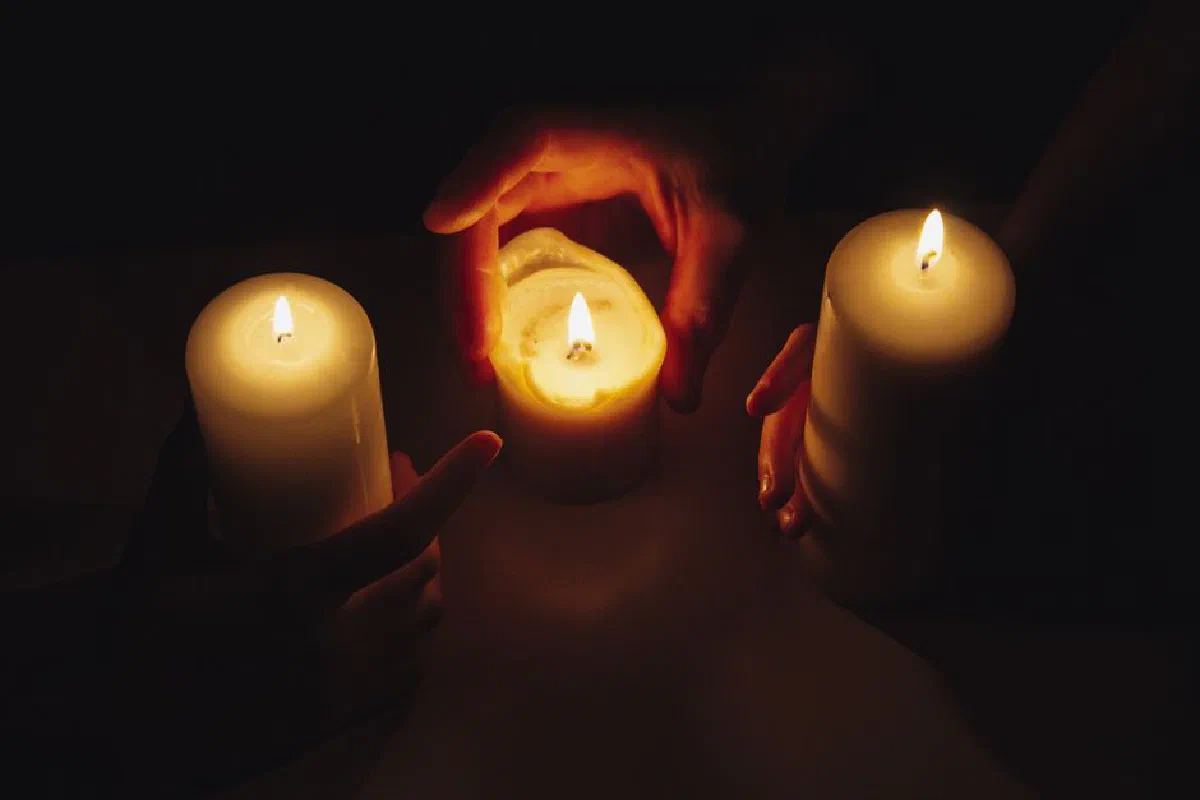 Hands holding burning candles in intimate, meditative candlelight.