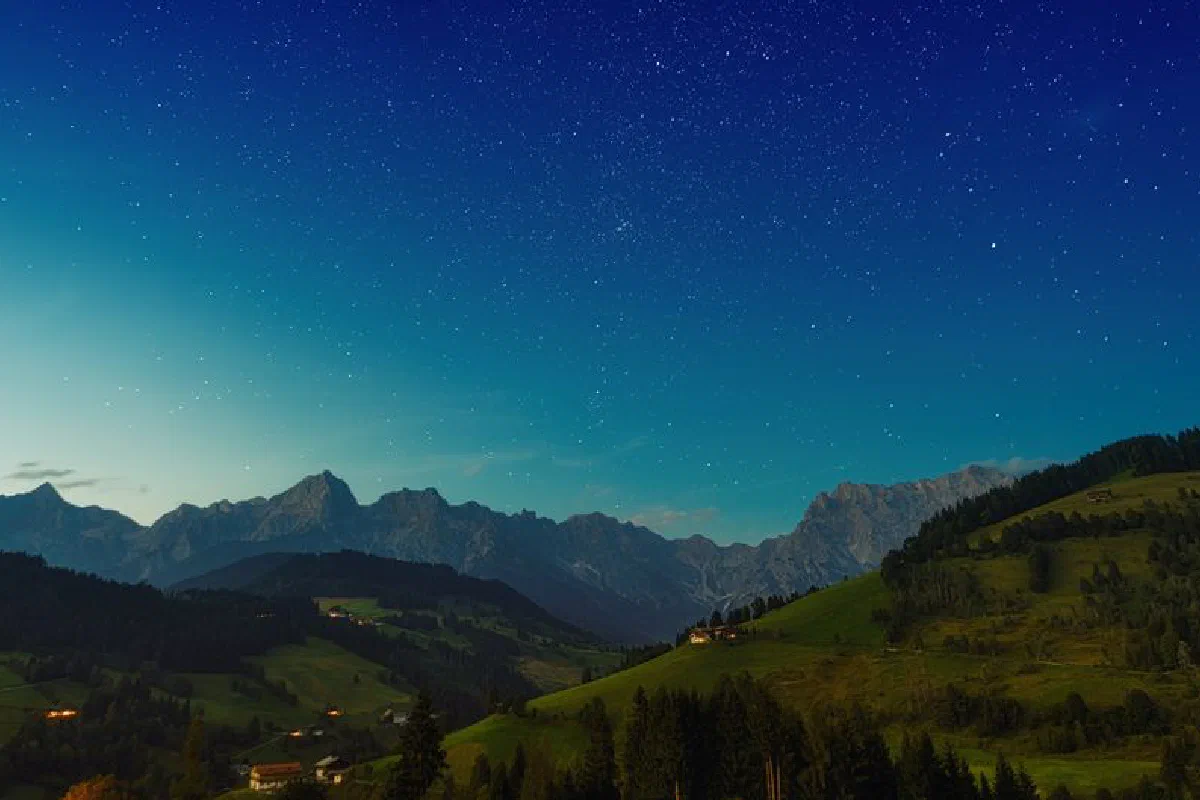 Picturesque green grassy hills located against cloudless starry sky in evening in countryside