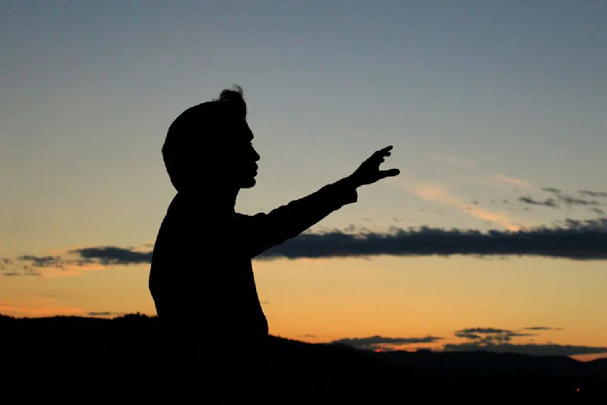 Silhouette of a person with raised hand against a vibrant sunset sky, creating a dramatic effect.