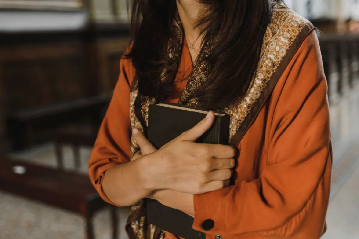 Close-up of a woman holding a book in a religious environment, symbolizing faith and spirituality.