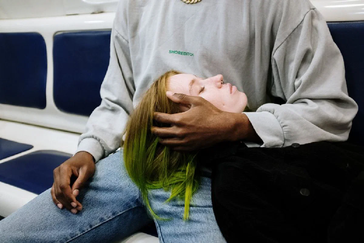Young couple with unique style resting on a subway ride, showcasing urban lifestyle.