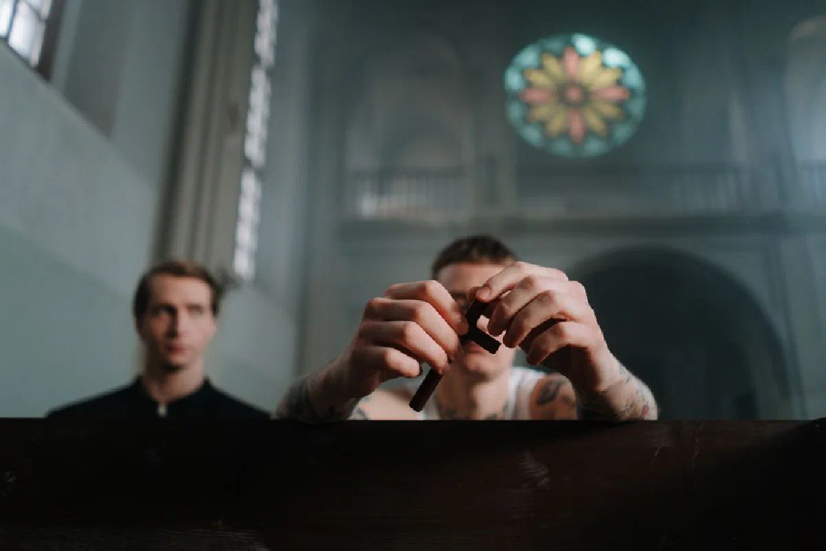 Two men praying inside a church, focusing on hands holding a crucifix