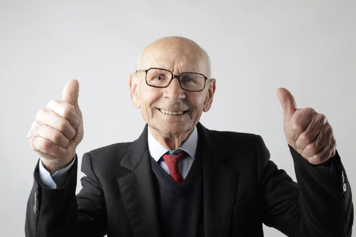 Optimistic senior man in elegant formal black suit and eyeglasses standing and showing thumbs up while smiling and looking at camera