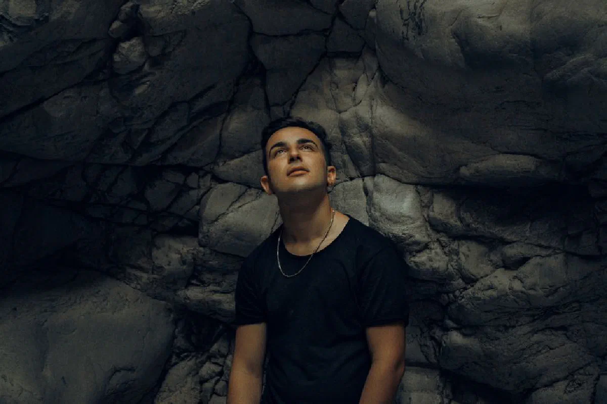 Serious young male traveler in casual clothes looking up while standing near rough rocky wall in ravine during trip in nature