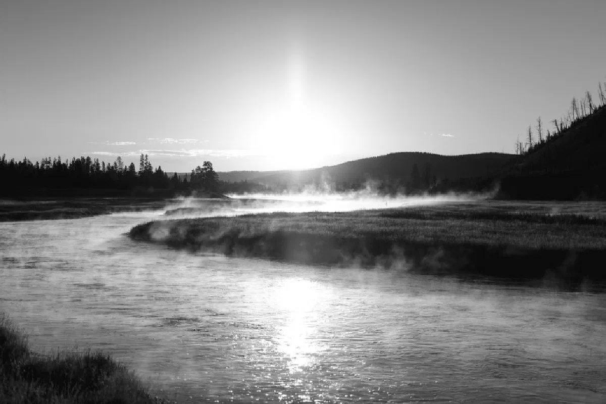 Black and white serene river landscape with mist rising at sunrise.