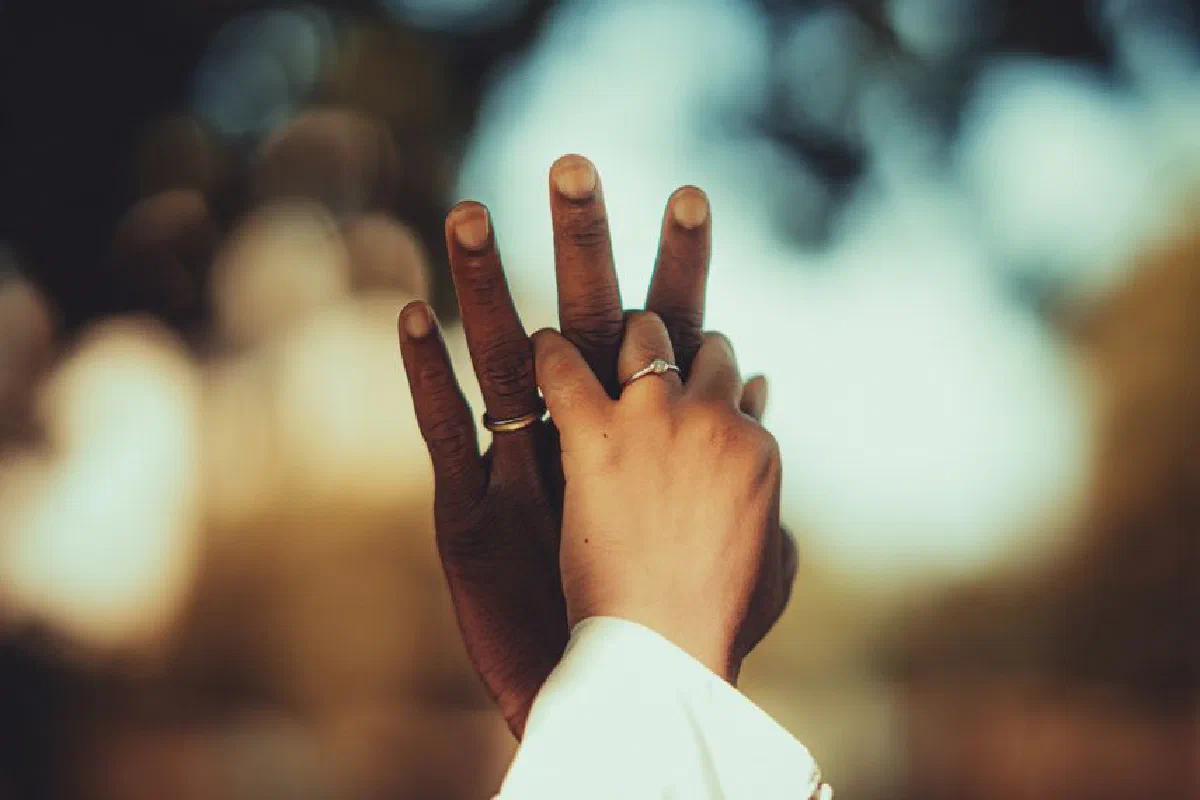 A close-up of hands interlocked, showcasing wedding rings, symbolizing love and unity outdoors.