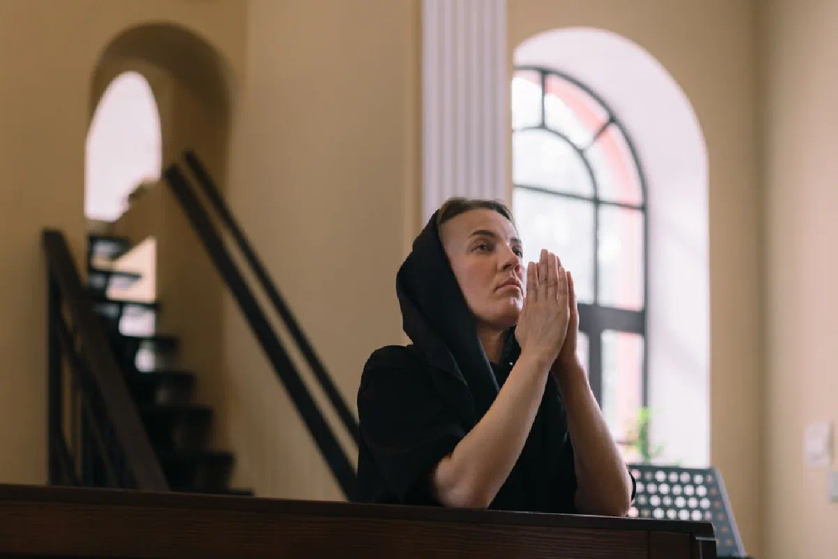 A woman in a headscarf prays inside a peaceful church, expressing devotion and spirituality.