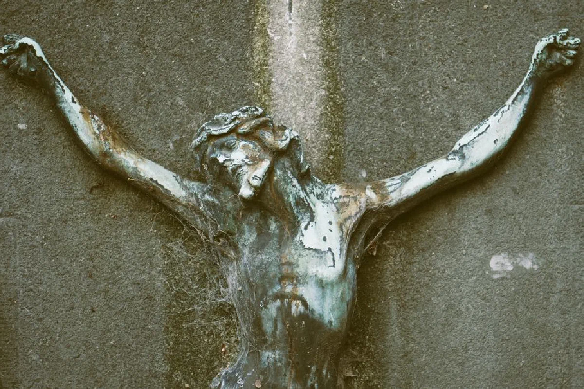 Detailed close-up of a weathered crucifix sculpture on a textured wall.