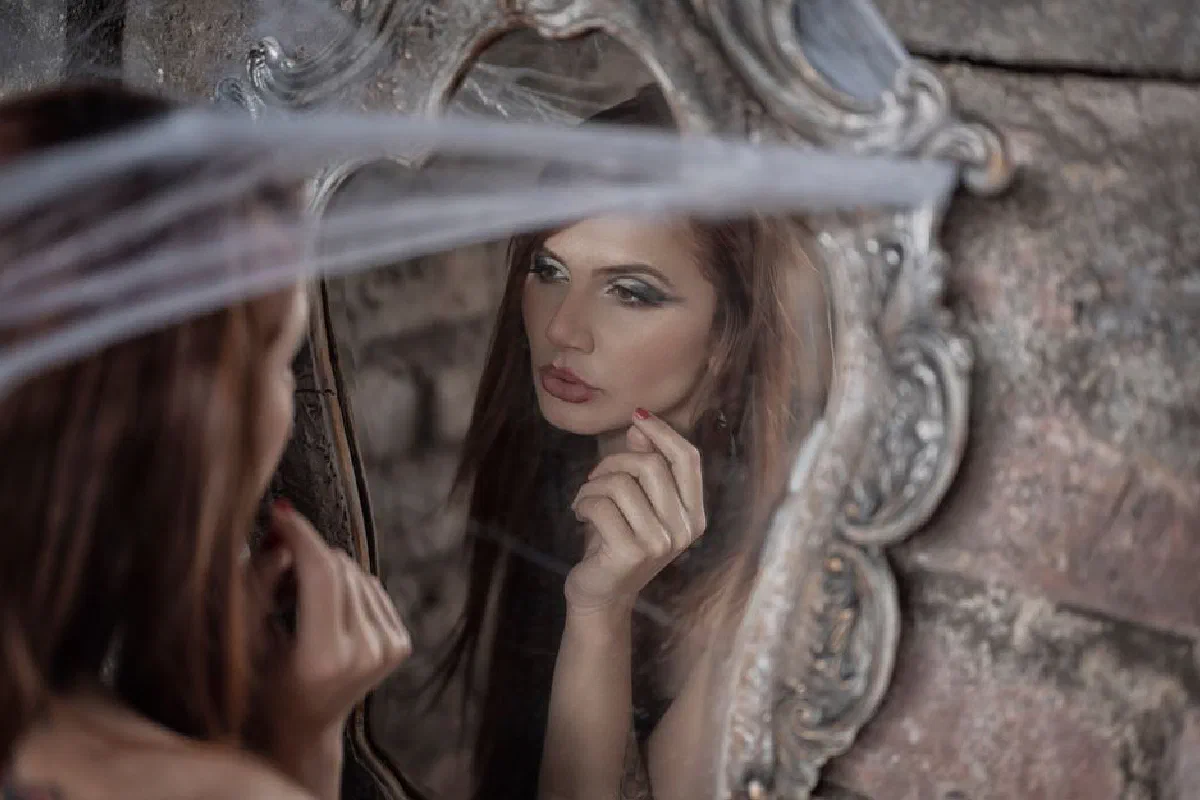 A young woman gazes at herself in an ornate mirror, creating a thoughtful reflection.
