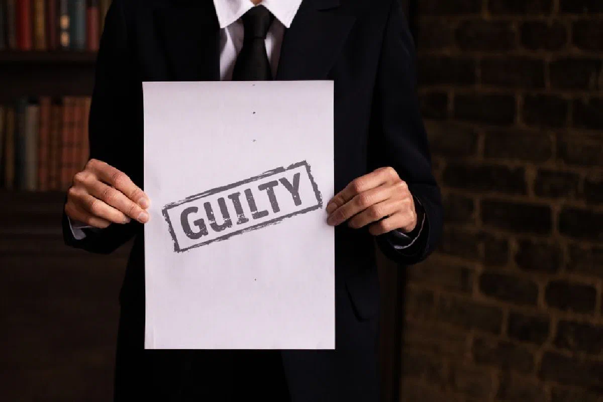 A businessman in a formal suit holding a sign with the word 'GUILTY.'