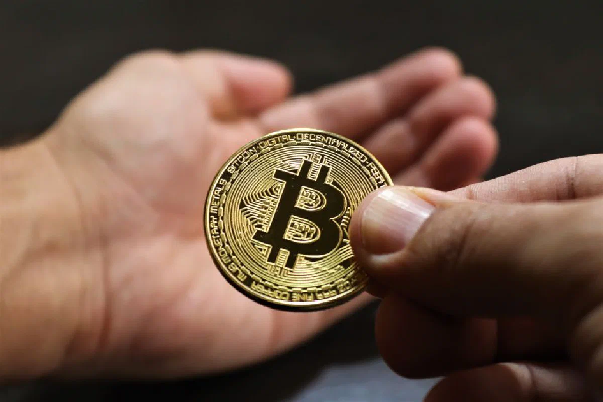 Close-up image showing hands exchanging a Bitcoin coin, symbolizing cryptocurrency transactions.