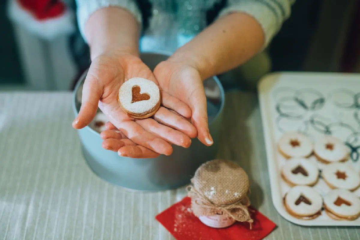 Close-up of hands holding freshly baked heart-shaped cookies dusted with powdered sugar.