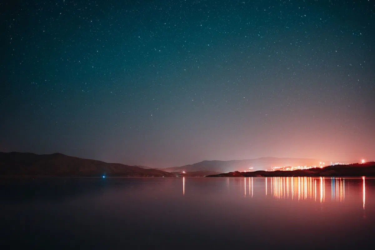 Tranquil nightscape with starry sky and mountain reflections in a serene lake.