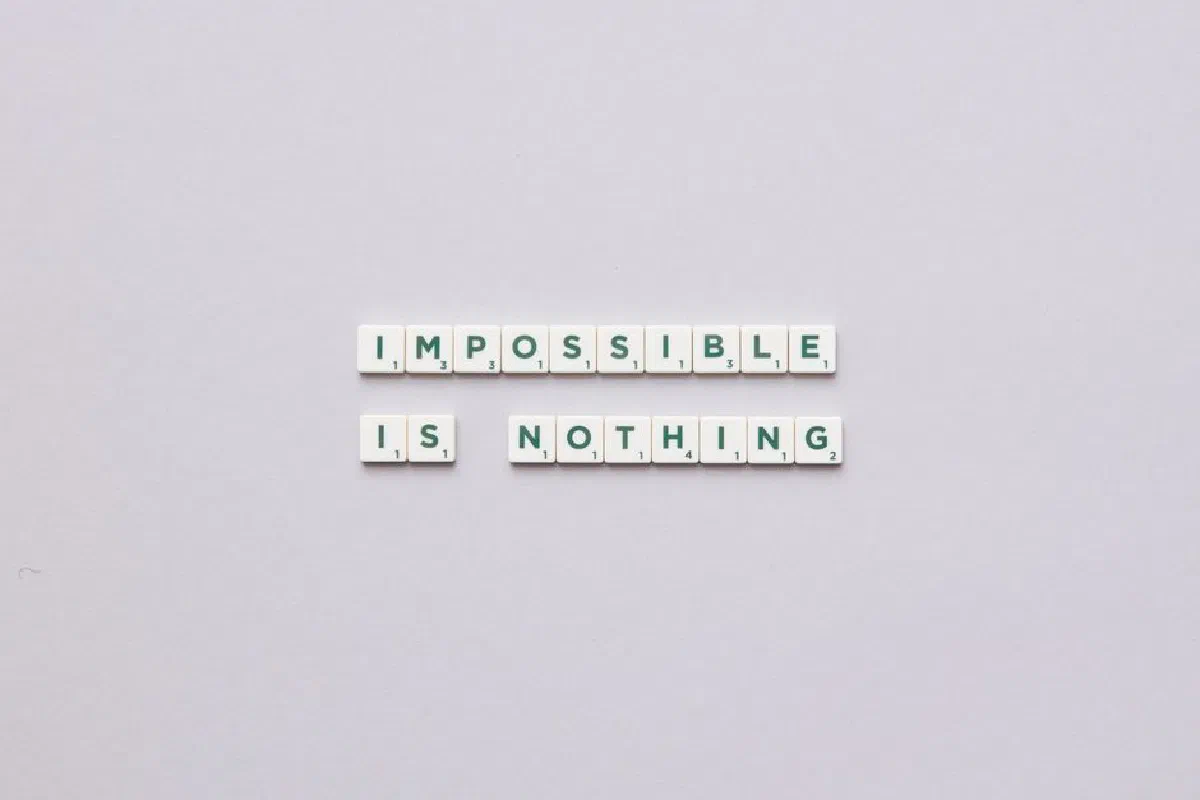 Flat lay of Scrabble tiles spelling 'Impossible is Nothing' on a neutral background.