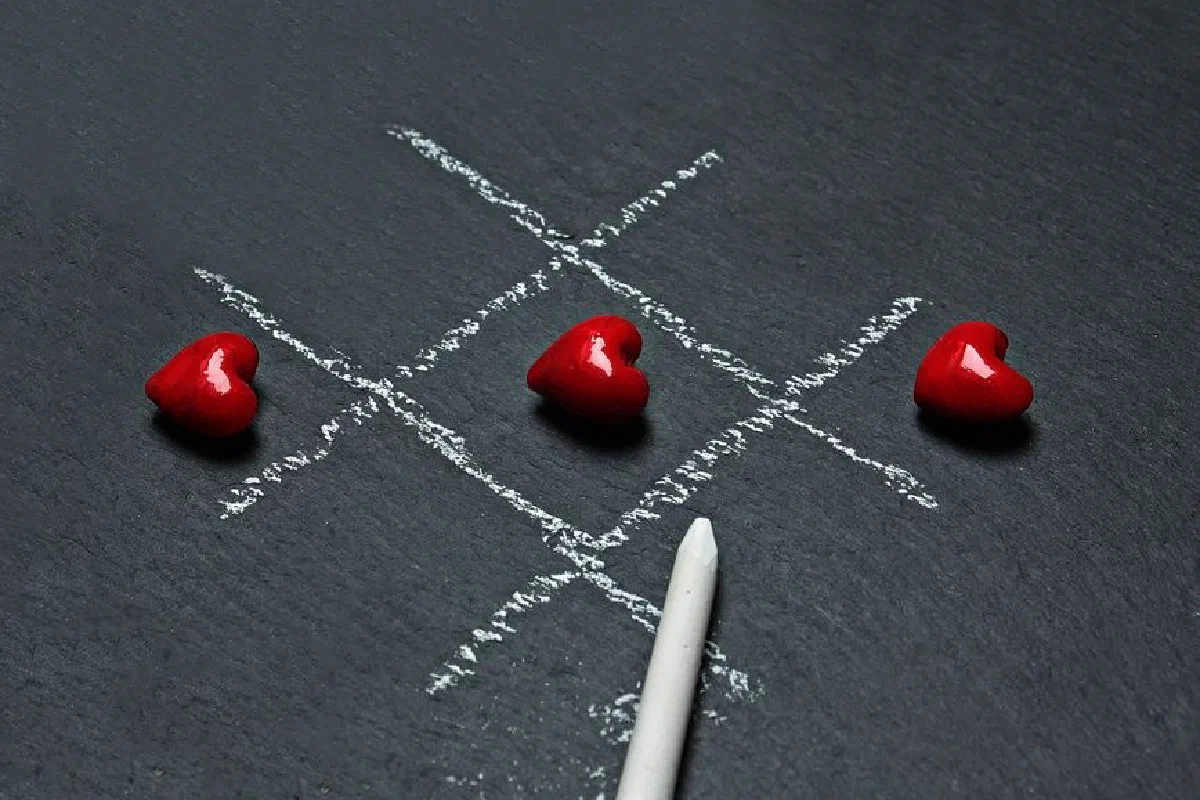 Creative tic tac toe game using red heart symbols on a chalkboard.