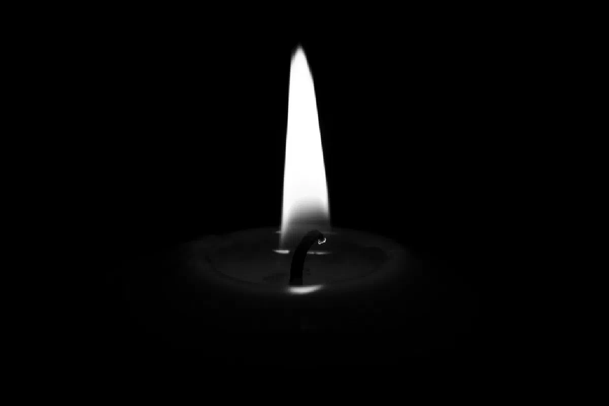 A black and white close-up of a candle with a burning wick against a dark background.