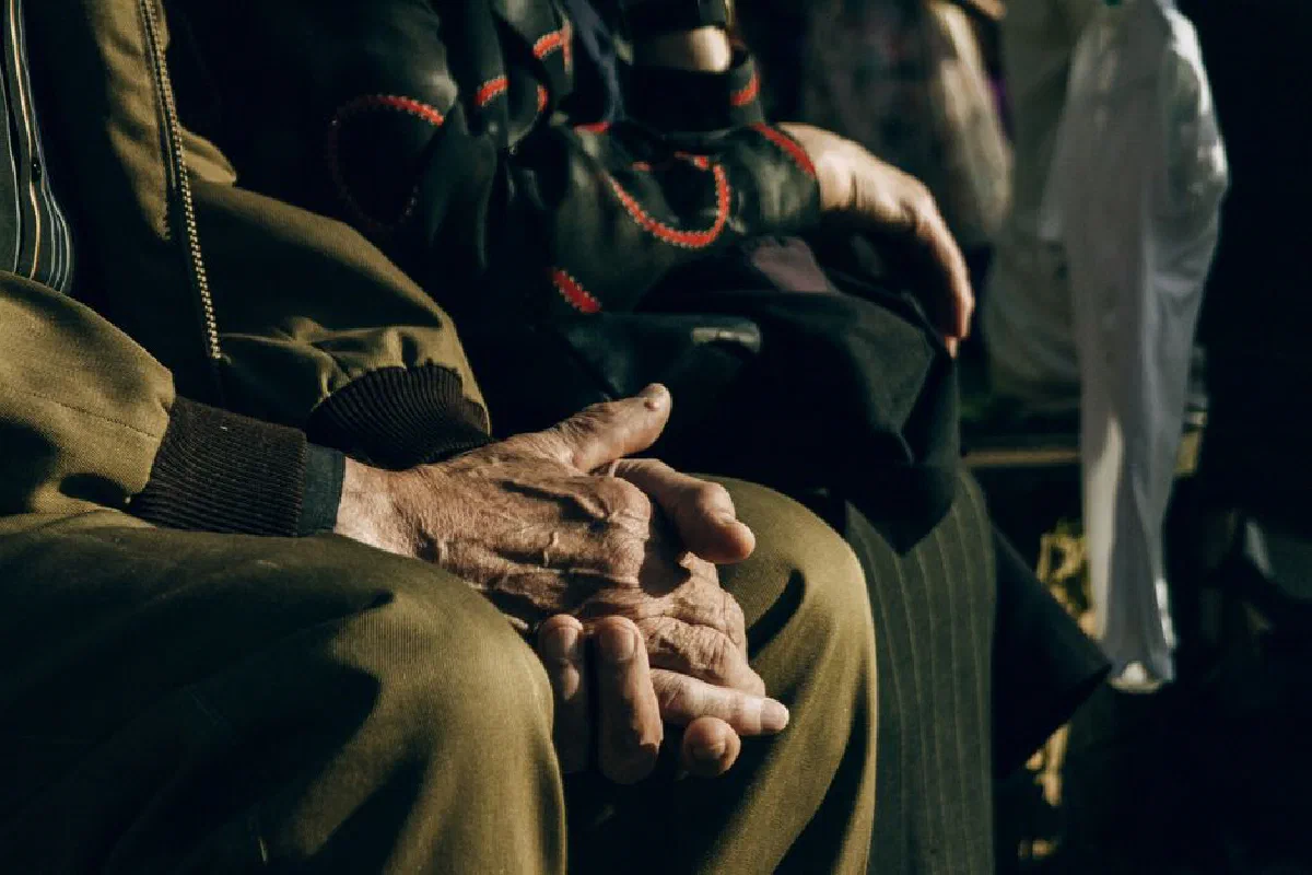 Hands of elderly people resting on their laps at an outdoor gathering.