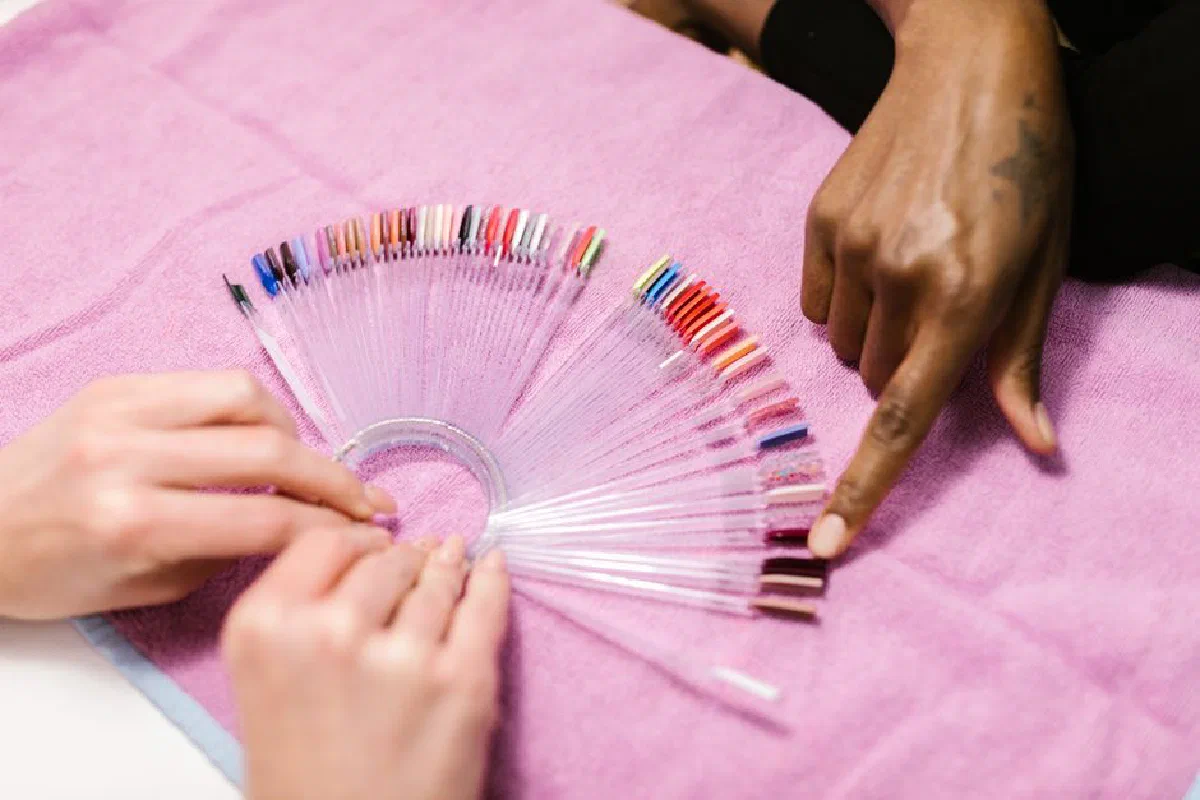 Hands selecting nail polish shades on color palette at salon. Manicure selection process.