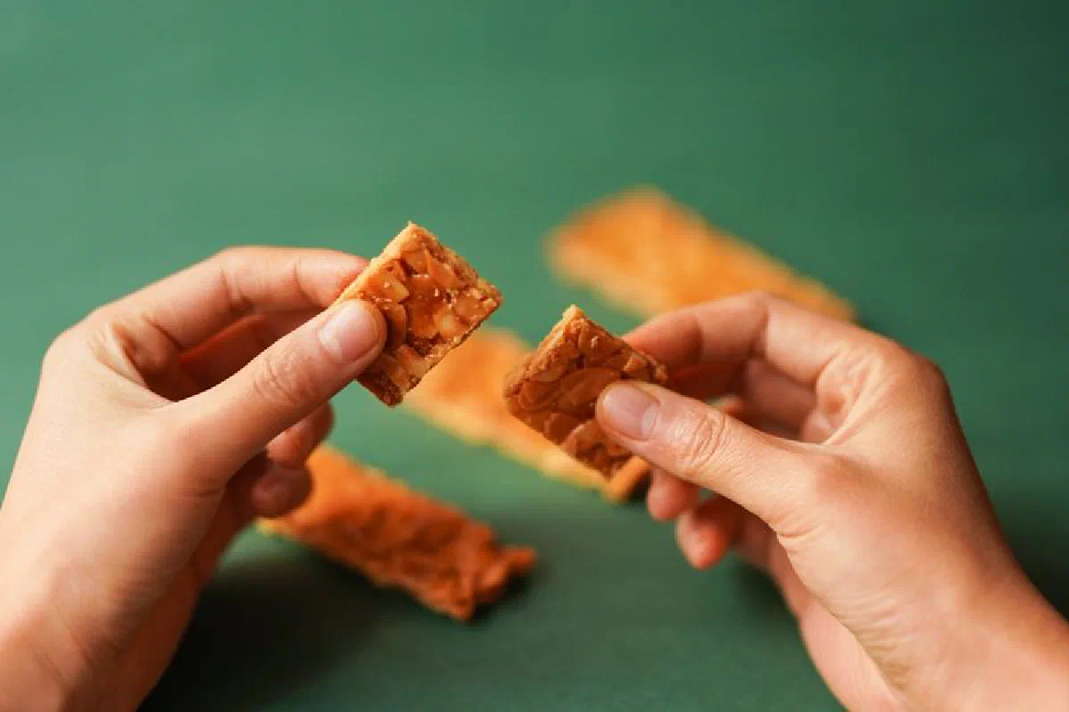 Close-up of hands holding crispy nut cookies on a green background.