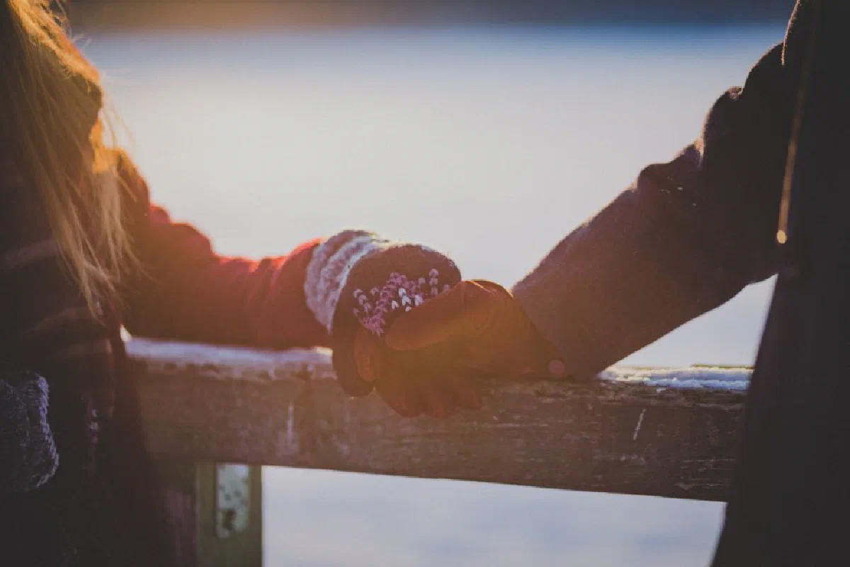 Two people holding hands warmly in a scenic winter backdrop during sunset.