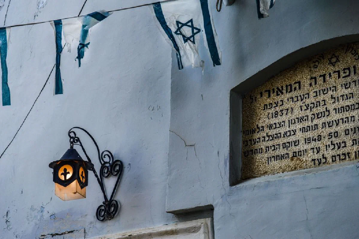 Close-up of an illuminated wall lamp beside a Hebrew inscription, adorned with Israeli flags.