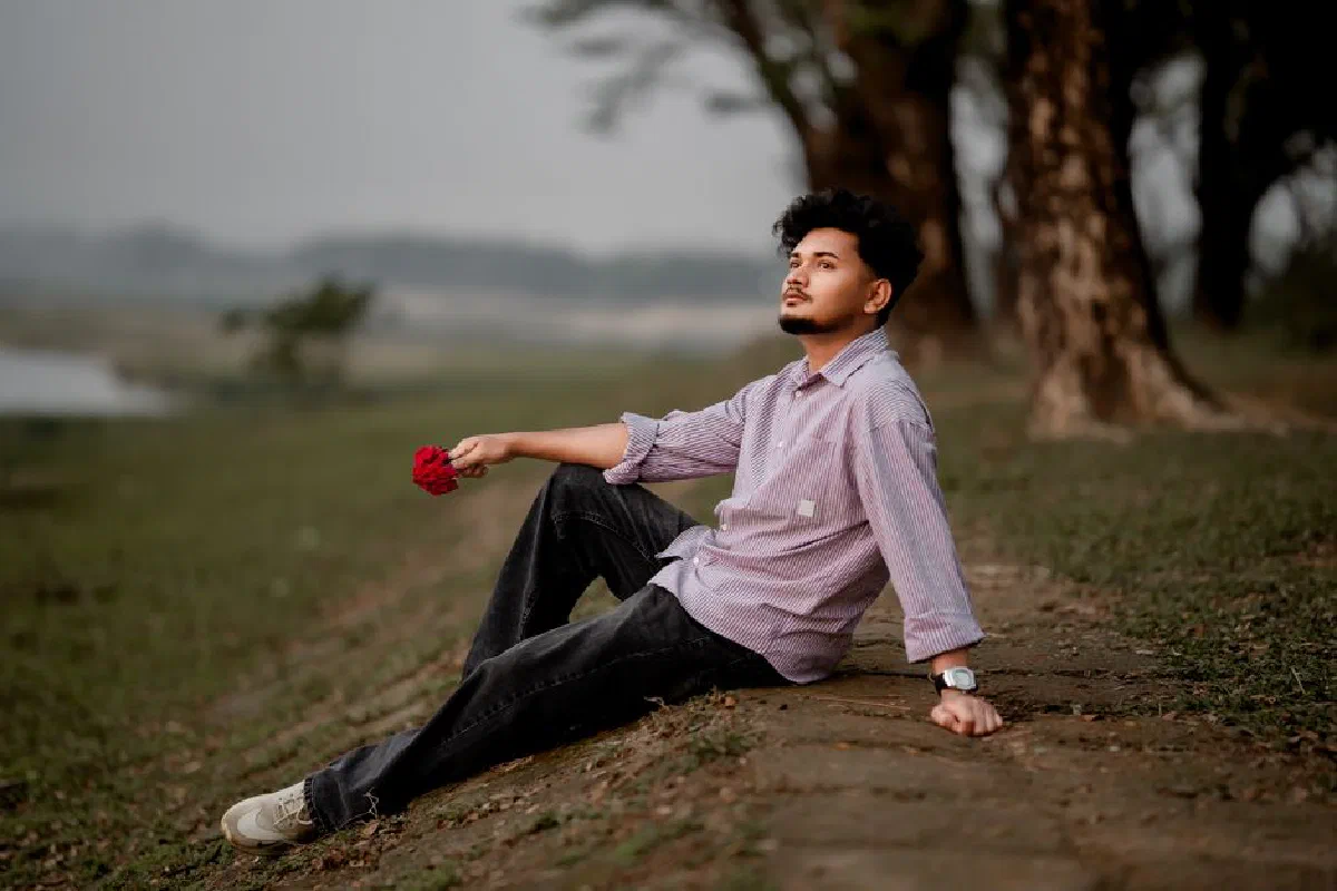 A thoughtful man sits outside holding a flower, exuding a peaceful vibe in Bangladesh.
