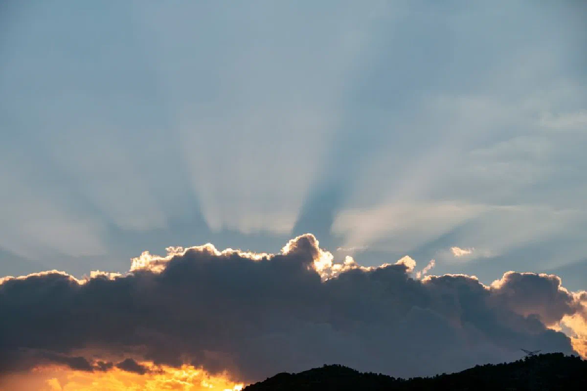 Sunbeams piercing through thick clouds at sunset, creating a dramatic sky.
