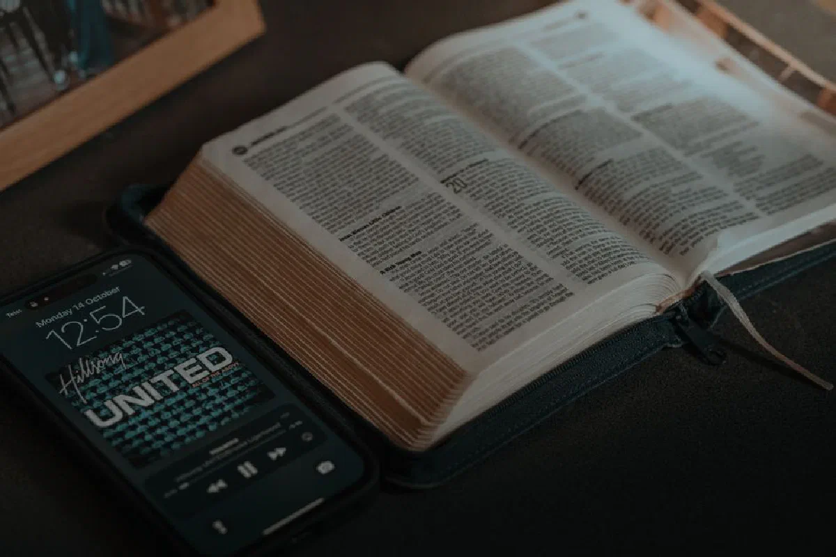 Open Bible on a table next to a smartphone displaying a playlist, conveying a spiritual and modern theme.