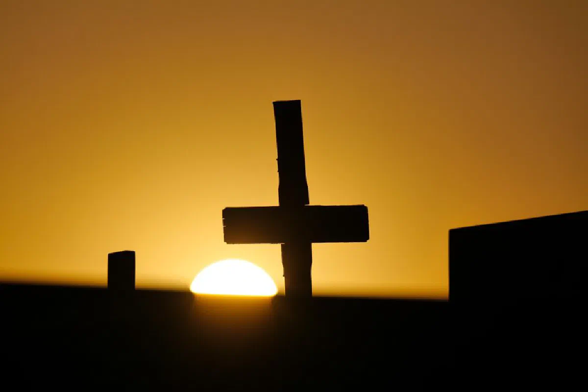 Silhouette of a cross against a golden sunset in Garešnica cemetery, reflecting religious themes.