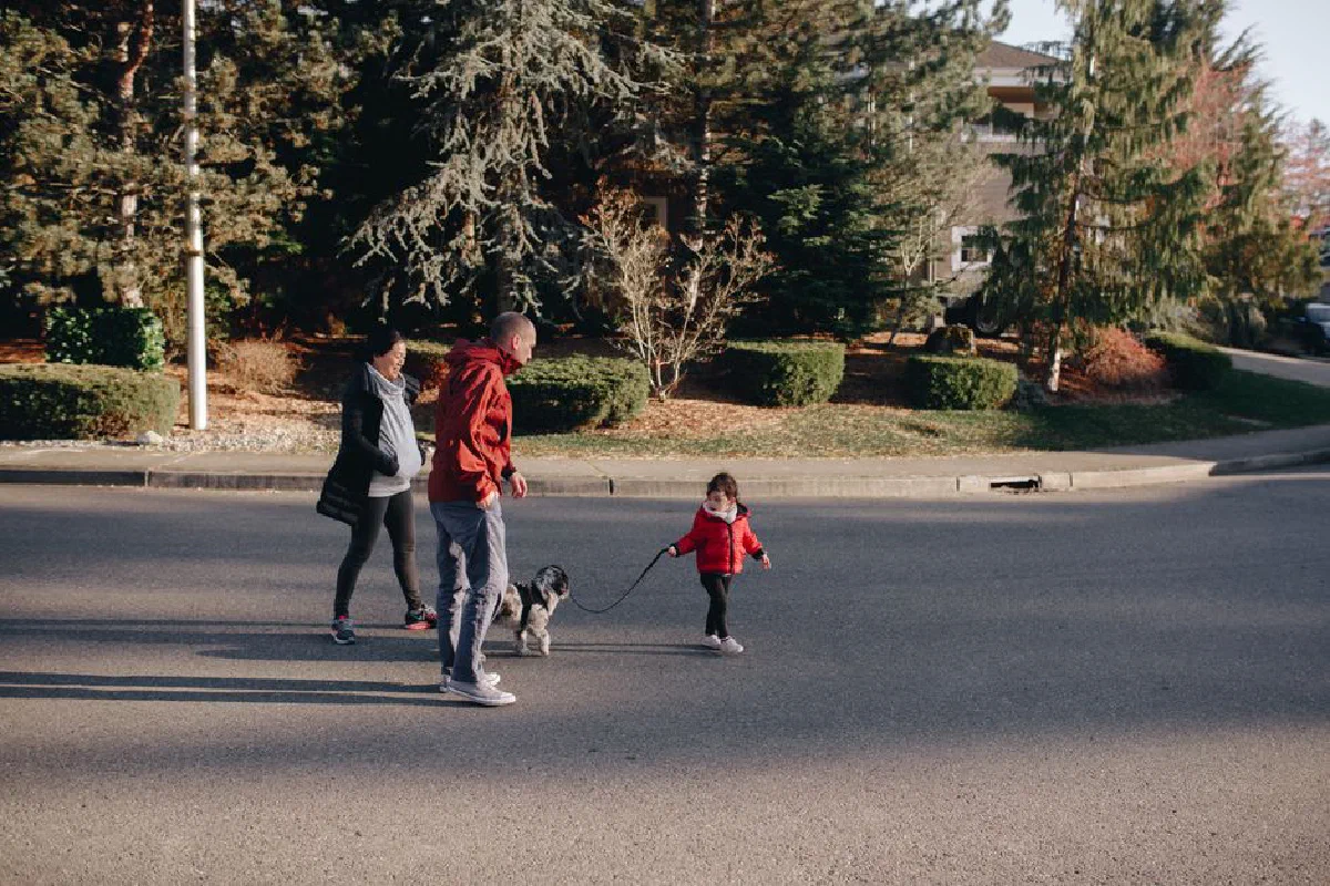 Family enjoying a sunny day walk with their dog in a suburban neighborhood.