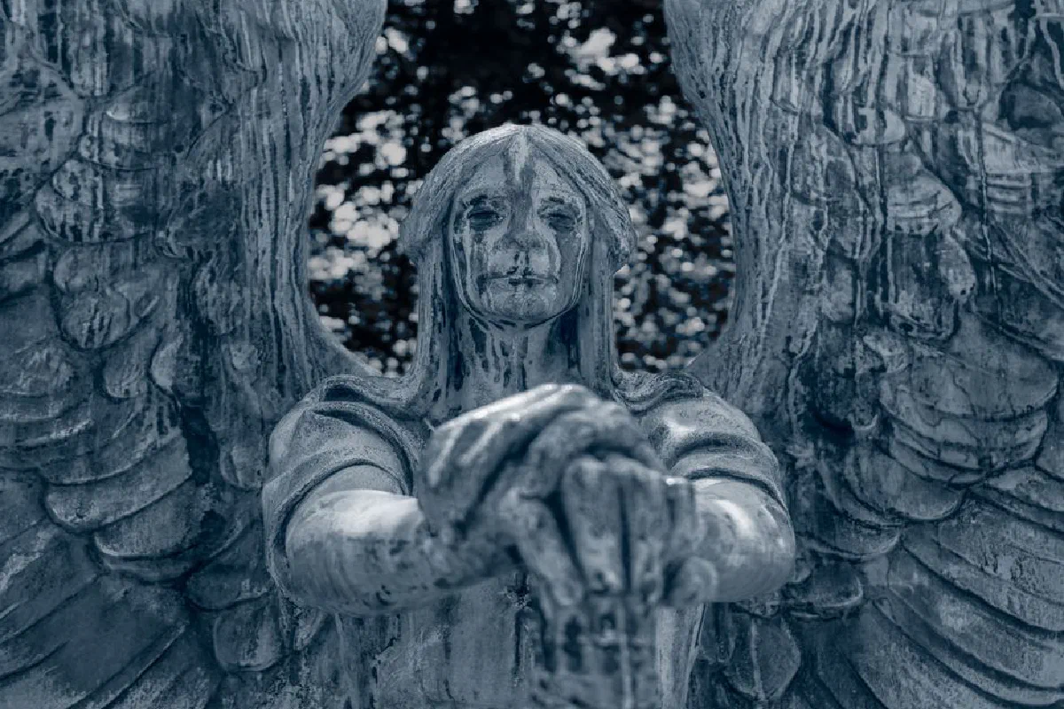 Close-up of an aged stone angel statue with a solemn expression in a moody and dramatic setting.