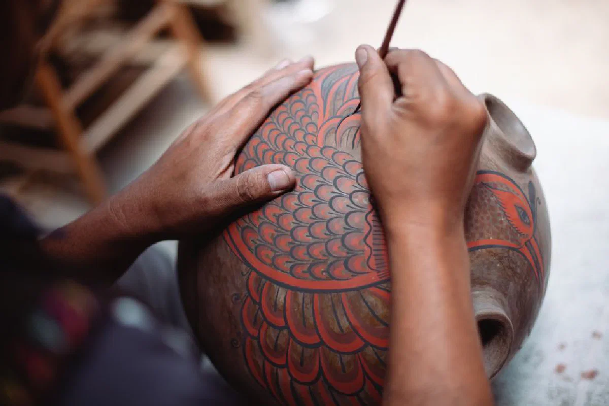 Close-up of artisan painting intricate designs on a ceramic pot in a traditional workshop.