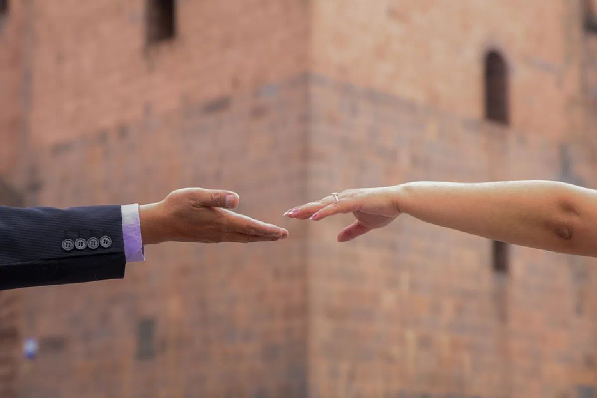 Close-up of hands reaching toward each other in front of a brick wall, symbolizes connection.