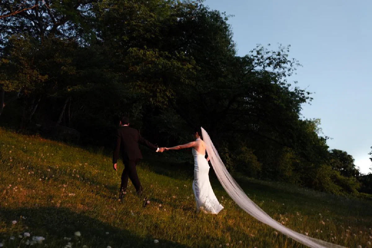 A couple in wedding attire strolls through a sunlit park, embracing love and nature.